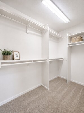 A clean, white closet with open shelving and a hanging rod, featuring a plant and a framed picture on the top shelf. - Luxury Furnished Home - 90 Day Minimum Stay (Lincoln)