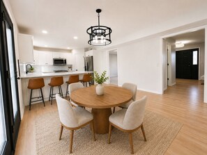 A modern kitchen with white cabinets, a central island, and a dining area with a round table and chairs. - Luxury Furnished Home - 90 Day Minimum Stay (Lincoln)