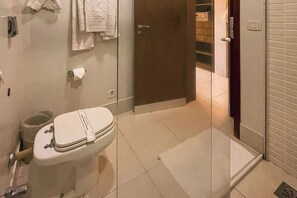 Ein Badezimmer mit Toilette, einer Duschkabine aus Glas und einem Handtuchhalter mit gefalteten Handtüchern.