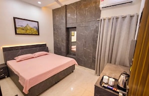Habitación de hotel con una cama, una mesita con un hervidor, tazas y una bandeja, un cuadro en la pared y una cortina.