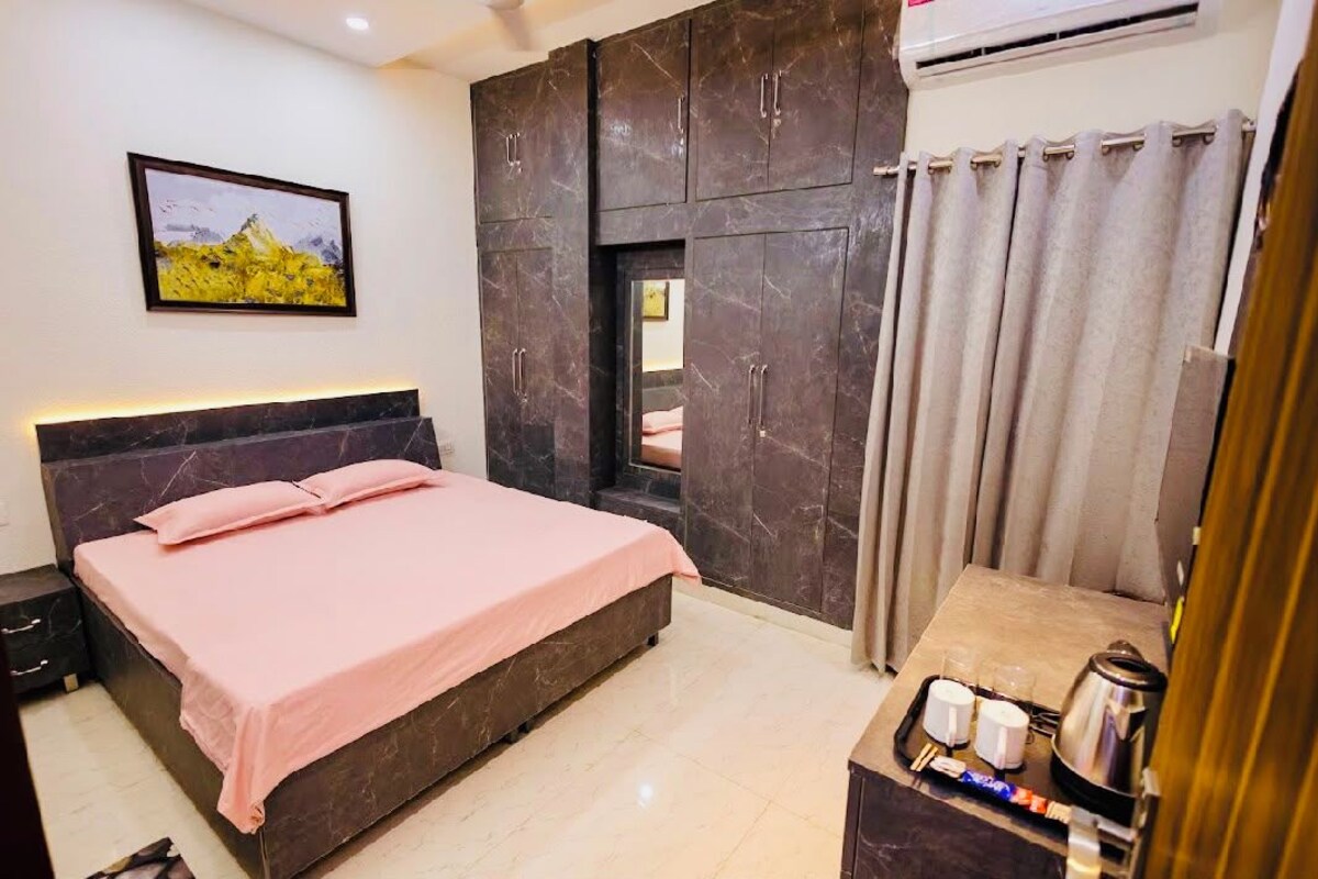 Un dormitorio con cama, armario, mesita de noche con tetera y ventana con cortinas.