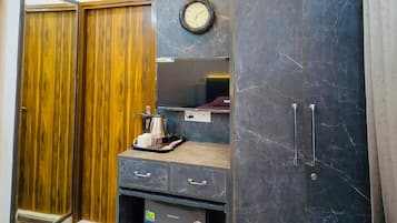A compact room with a wardrobe, a small kitchenette, a clock, and a ceiling light fixture.