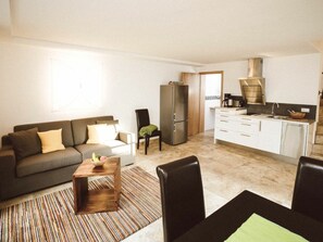 A compact living space with a sofa, a coffee table, a dining table, and a kitchen area. - Luna Mia 1/chalet (Schwangau)