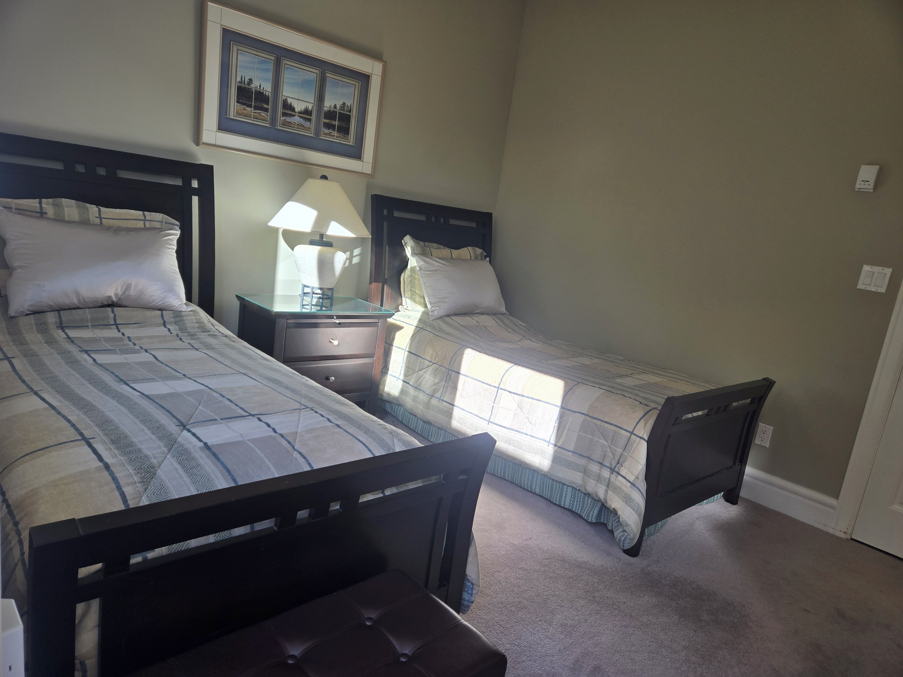 A bedroom with two beds, a nightstand, a lamp, and a framed picture on the wall.