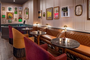 Un espacio lounge moderno con asientos de cuero, mesas redondas pequeñas y obras de arte colgadas en la pared.