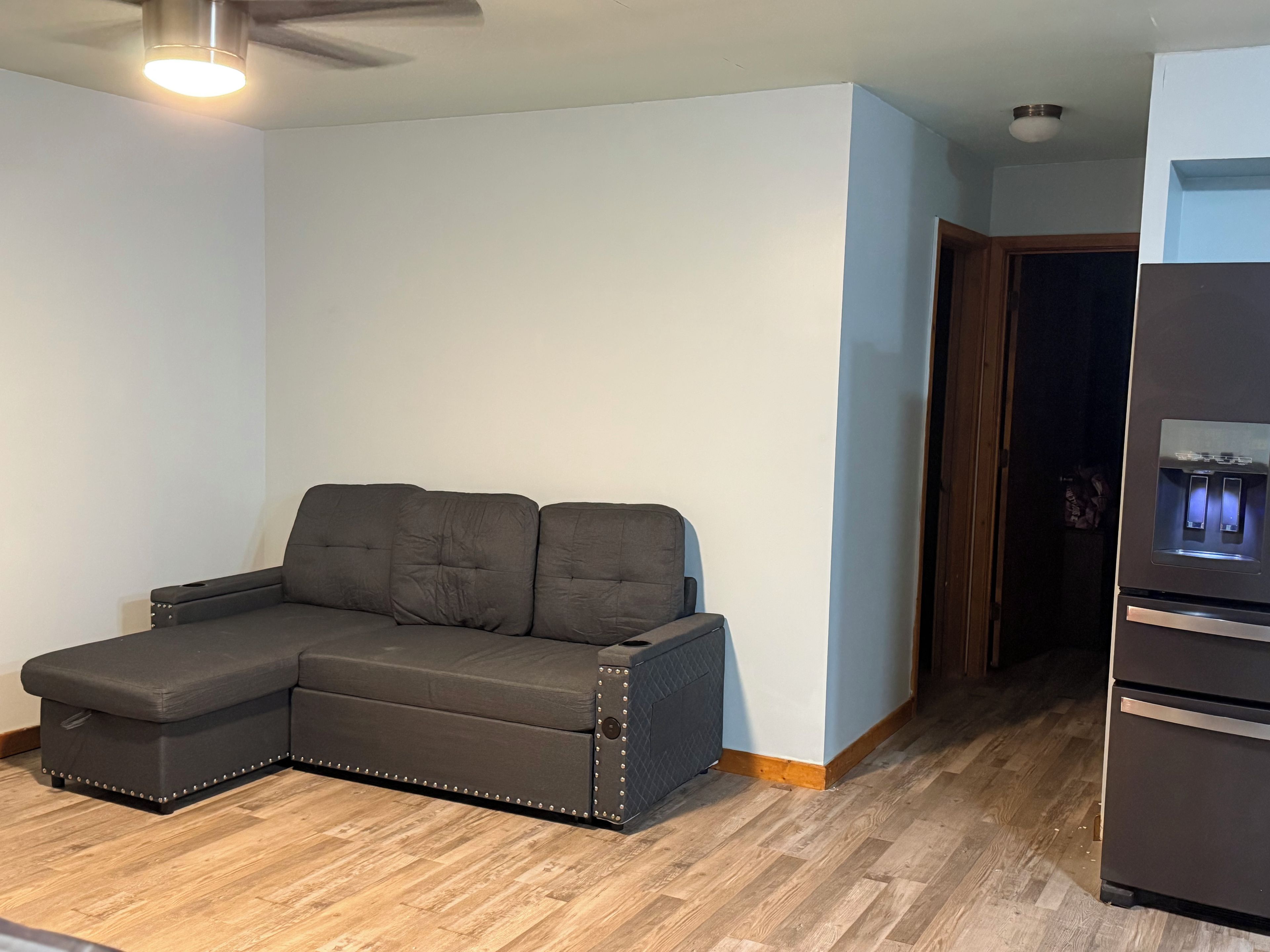 Una habitación con sofá modular, ventilador de techo y refrigerador.