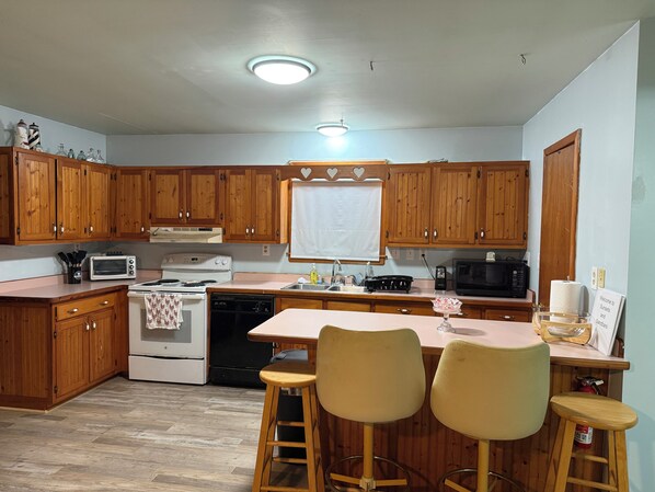 A kitchen with wooden cabinets, a stove, a microwave, and two bar stools.