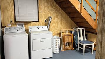 Ein Waschraum mit zwei Waschmaschinen, einem Wäscheständer, einem Stuhl und einem Fenster mit Jalousien.