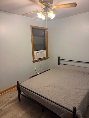 A bedroom with a bed, a ceiling fan, a window with blinds, and a wall-mounted air conditioner.