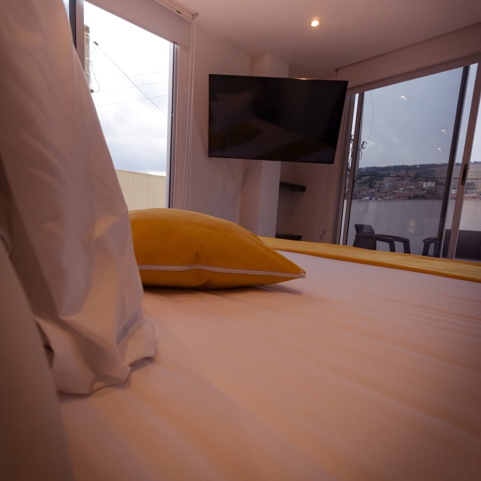 Une chambre d’hôtel avec un lit, un téléviseur fixé au mur et une vue sur le paysage urbain, visible à travers de grandes fenêtres.