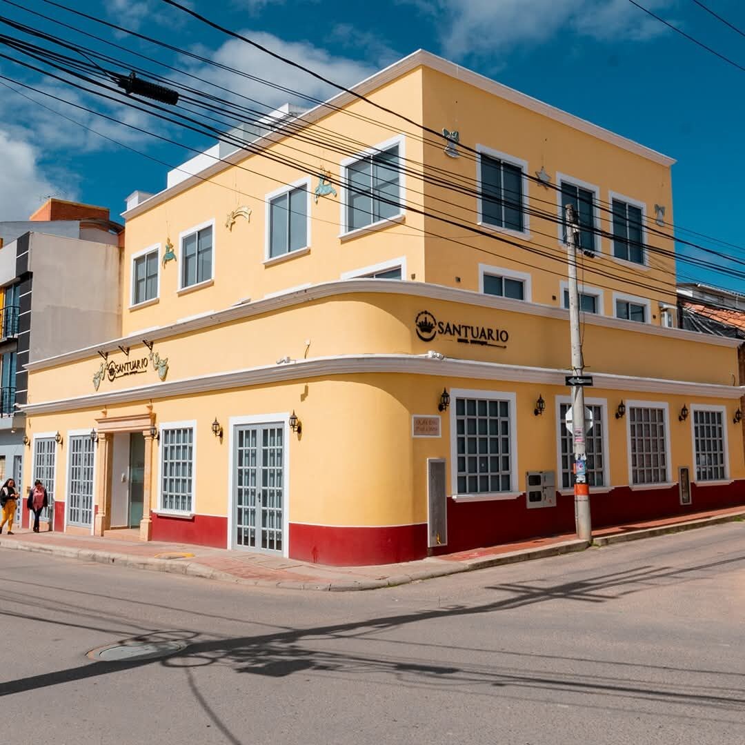 A two-story building with a yellow facade and a red base, featuring a sign that reads 'SANTUARIO.'