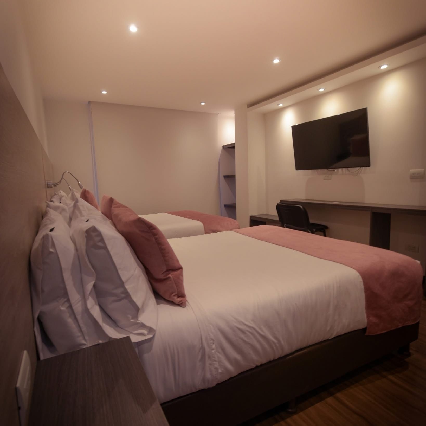 Une chambre d’hôtel avec deux lits, un téléviseur à écran plat fixé au mur et un bureau avec une chaise.
