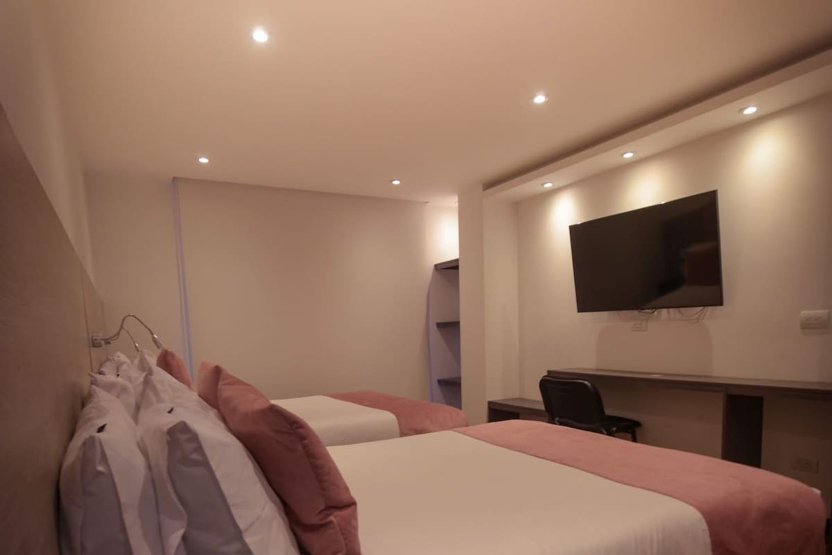 Et hotelværelse med to senge, et fladskærms-TV monteret på væggen og et skrivebord med stol.