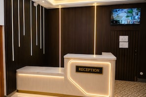 Una recepción con un cartel que dice 'RECEPTION', una cámara de seguridad instalada y un televisor de pantalla plana mostrando imágenes de seguridad.