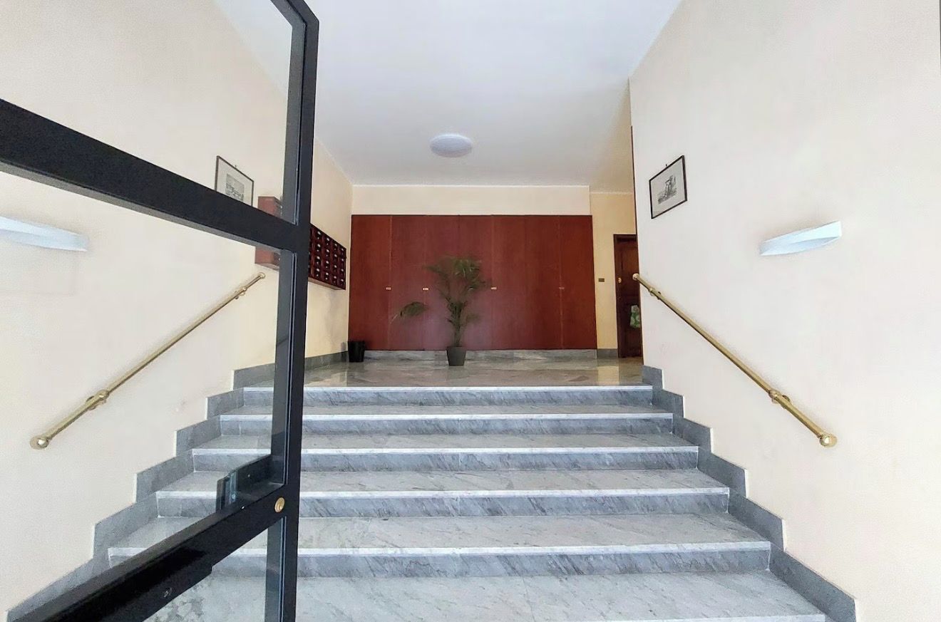 Una scala in marmo con ringhiere nere che conduce a una stanza con una porta in legno e una pianta in vaso.
