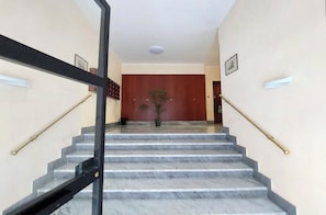 A marble staircase with black handrails leading to a room with a wooden door and a potted plant. - New Listing (Roma)
