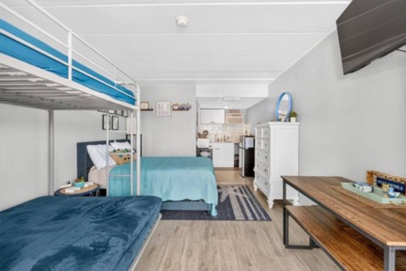Une pièce de taille modeste, équipée de lits superposés, d’une petite kitchenette et d’une table en bois.