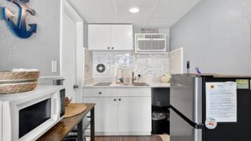 Cocina compacta con armarios blancos, microondas, refrigerador y un pequeño comedor con mesa y sillas.