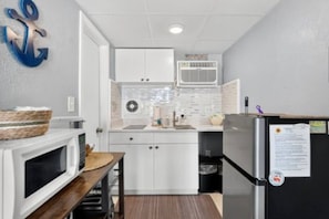 Cocina compacta con armarios blancos, microondas, refrigerador y un pequeño comedor con mesa y sillas.