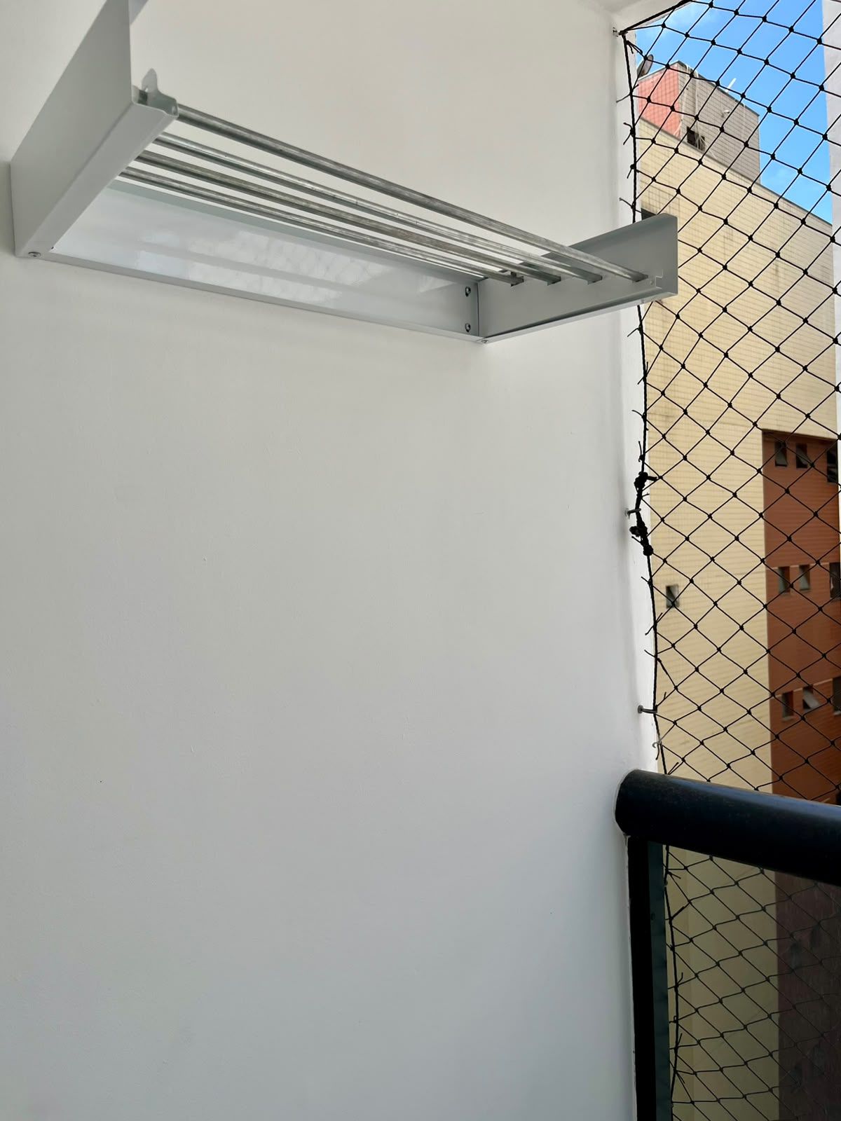 Eine weiße Wand mit einer Metall-Klimaanlage und einem Maschendrahtzaun.