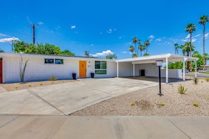 A single-story building with a covered patio area, a small front yard with gravel and plants, and a clear blue sky. - Thoughtfully Refreshed MCM.  3 Beds with Pool.  28+ day Rentals (Palm Desert)