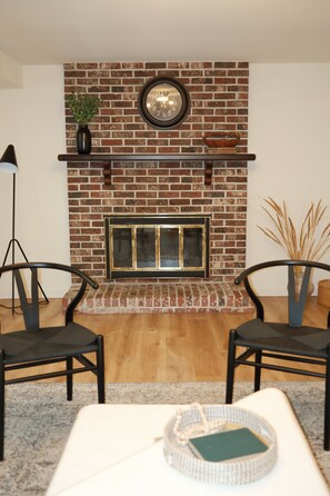 A living room with a brick fireplace, two chairs, a table with a tray, and a floor lamp. - Private 2 Bed ADU Near Airport & Hospitals (Kent)