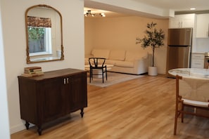 A living room with a wooden cabinet, a sofa, a dining table with chairs, and a potted plant. - Private 2 Bed ADU Near Airport & Hospitals (Kent)