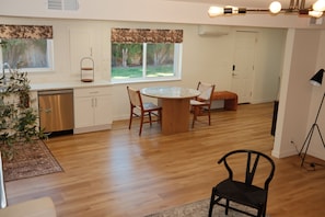 A modern kitchen with a dishwasher, a dining table with chairs, and a view of the outdoors through large windows. - Private 2 Bed ADU Near Airport & Hospitals (Kent)