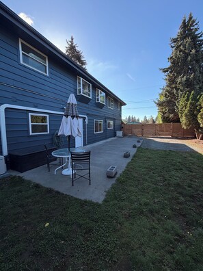 A residential backyard with a patio, a table, chairs, and a covered umbrella. - Private 2 Bed ADU Near Airport & Hospitals (Kent)