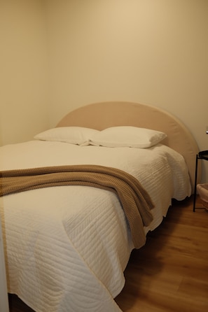 A neatly made bed with a white duvet and a brown throw blanket, positioned against a plain wall with a wooden floor. - Private 2 Bed ADU Near Airport & Hospitals (Kent)