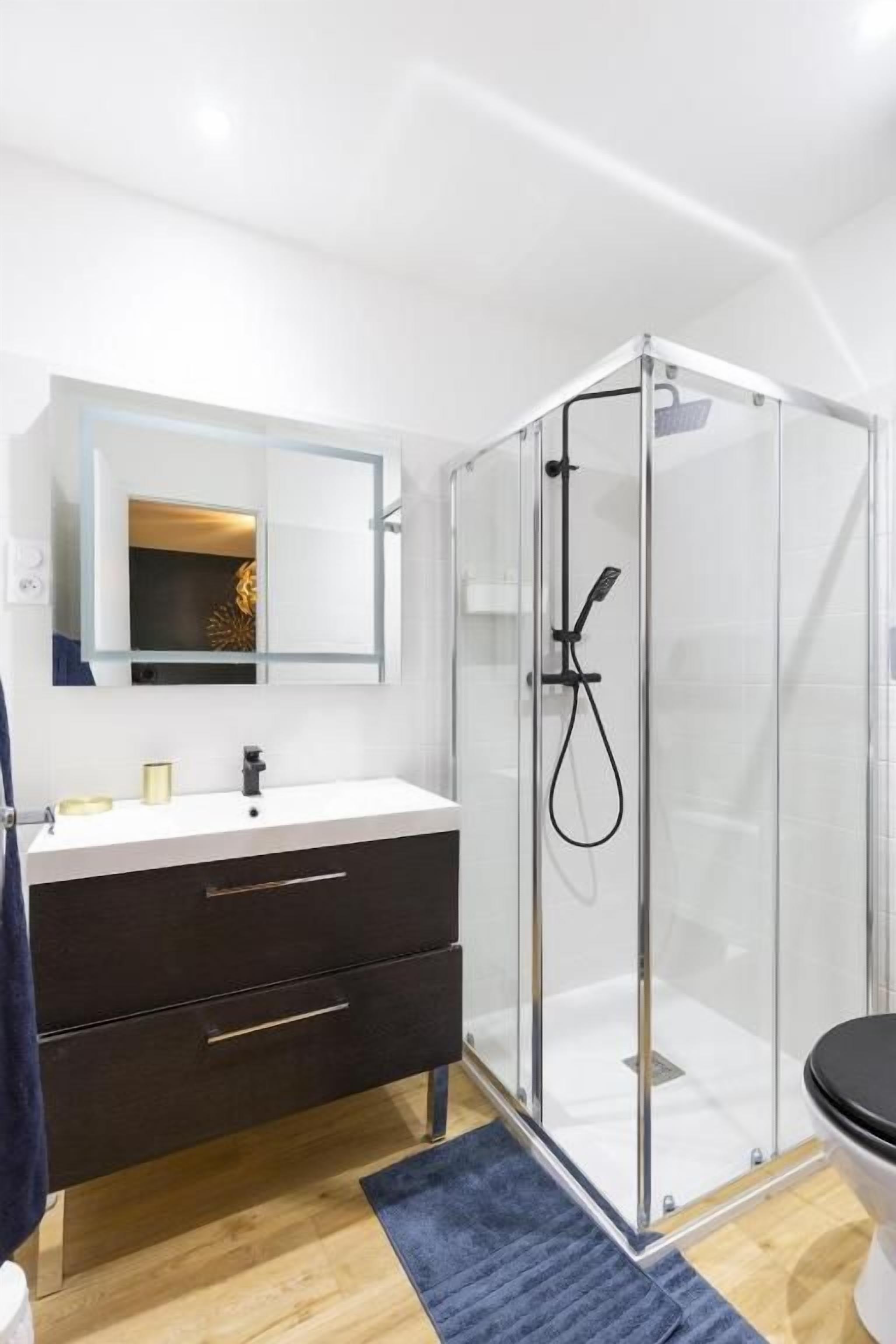 Une salle de bain moderne avec une douche à parois de verre, un lavabo blanc et un meuble-lavabo de couleur foncée.