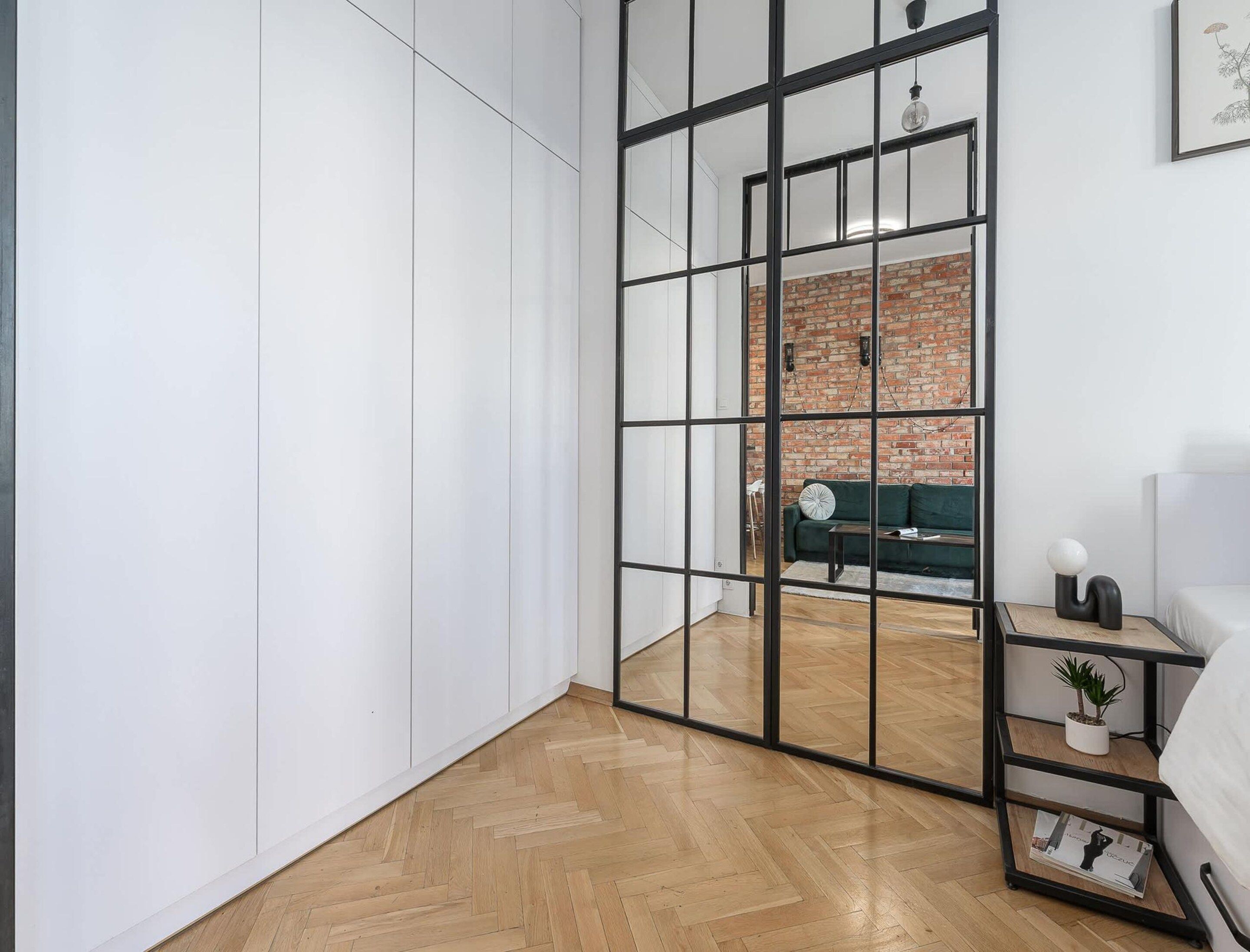 A room with a herringbone floor, a brick wall, a green sofa, and a white wardrobe.