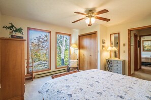 Un dormitorio con cama, ventilador de techo, ventana con vista a árboles y armario de madera.