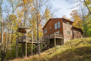 A wooden cabin with a deck and stairs, surrounded by trees with autumn foliage. - The Great Escape - Private Wooded Setting, Hot Tub & Babbling Brook! (Davis)