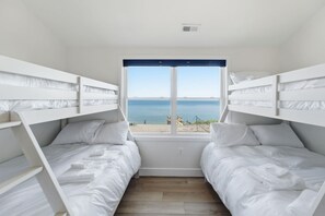 A room with bunk beds, a window with a view of the sea, and a wooden floor. - Luxury Beach Hs w/ 4 Suites, PrivateBeach & Htub (Heathsville)