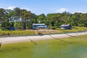 A beachfront property with multiple buildings, a sandy beach, and a forested area in the background. - Luxury Beach Hs w/ 4 Suites, PrivateBeach & Htub (Heathsville)