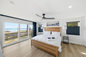 A bedroom with a wooden bed, a ceiling fan, and a view of the beach through large sliding doors. - Luxury Beach Hs w/ 4 Suites, PrivateBeach & Htub (Heathsville)
