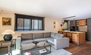Una sala de estar moderna con un sofá seccional gris, una mesa de centro y una cocina con armarios de madera y encimera negra.