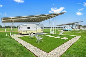 A recreational vehicle (RV) under a covered area with a lawn and seating. - Blue Skies Resort | Glamping | Pool | Fireplace (Fredericksburg)