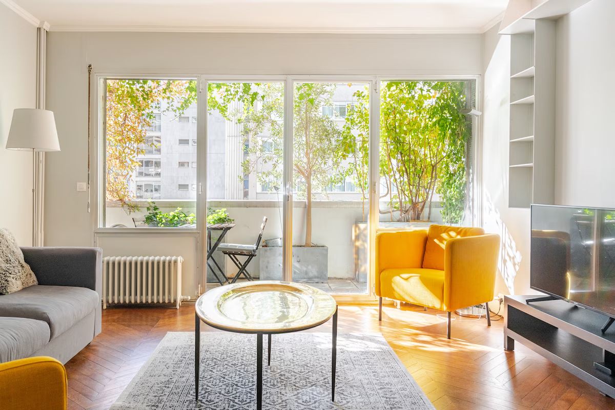 A modern living room with a sofa, a yellow armchair, a glass coffee table, and a television.