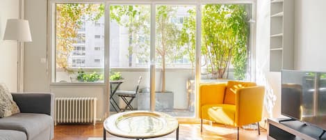 A modern living room with a sofa, a yellow armchair, a glass coffee table, and a television.