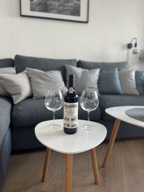 A bottle of wine on a white table with two glasses, a grey sofa, and a framed picture on the wall. - Ferienwohnung Bergpanorama - 5 minutes to the bike park and ski lift (Winterberg)