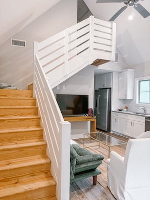 A modern kitchen with white cabinets, a stainless steel refrigerator, and a dining area with a glass table and green sofa.