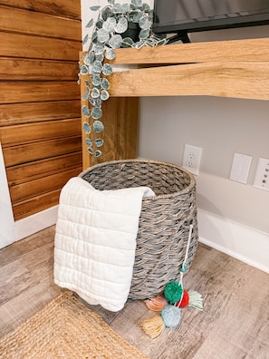 A corner of a room with a woven basket, a white quilted blanket, and a small rug on the floor. - Loveliest Cottage in Auburn (Auburn)