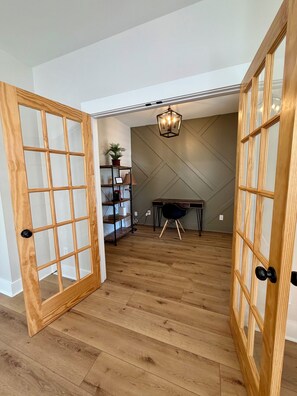 A room with wooden flooring, a desk, a chair, a hanging light fixture, and a shelving unit with a plant. - A modern relaxed retreat in charming historic downtown Springfield! (Springfield)