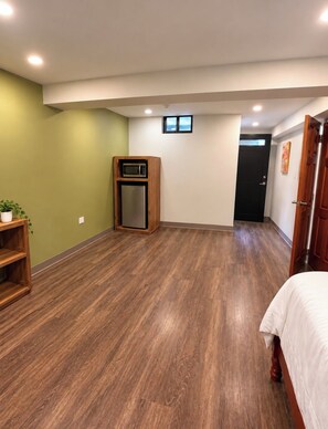 A room with a wooden floor, a built-in microwave, a refrigerator, a door, and a small window. - Lovely studio with AC in peaceful Lambeau (Lambeau)