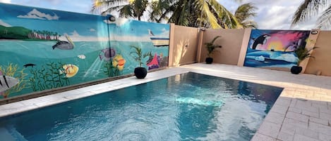 A swimming pool with tiled edges, surrounded by palm trees and a mural depicting underwater scenes.
