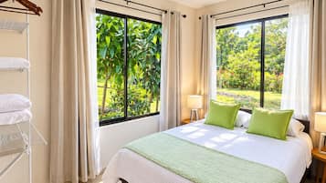 A bedroom with a bed, two bedside tables, a ceiling fan, and large windows with curtains.