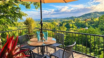 A terrace with a table and chairs, a table umbrella, and a view of a lush landscape.