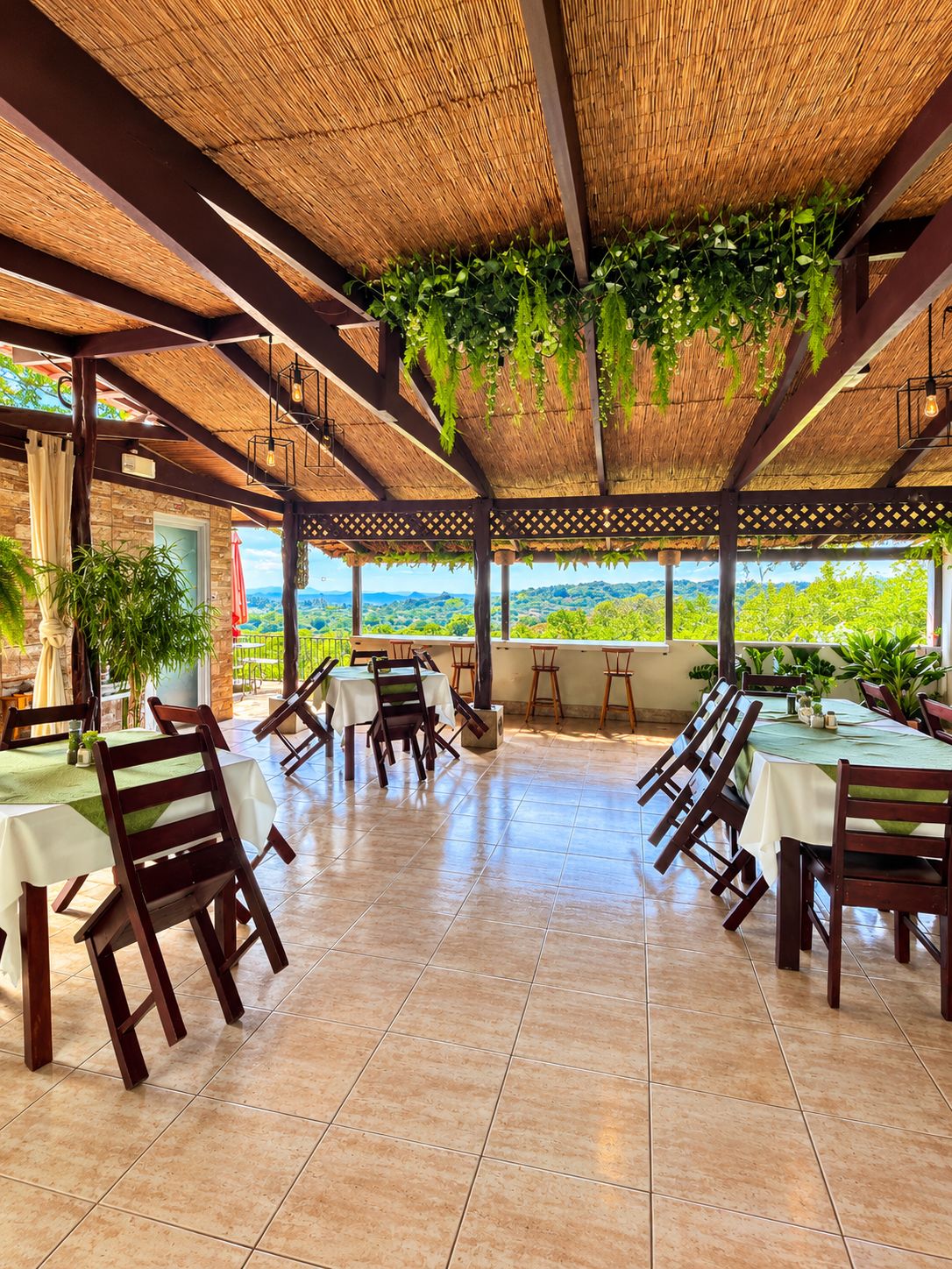 An outdoor dining area with tables and chairs, a thatched roof, and a view of the landscape.